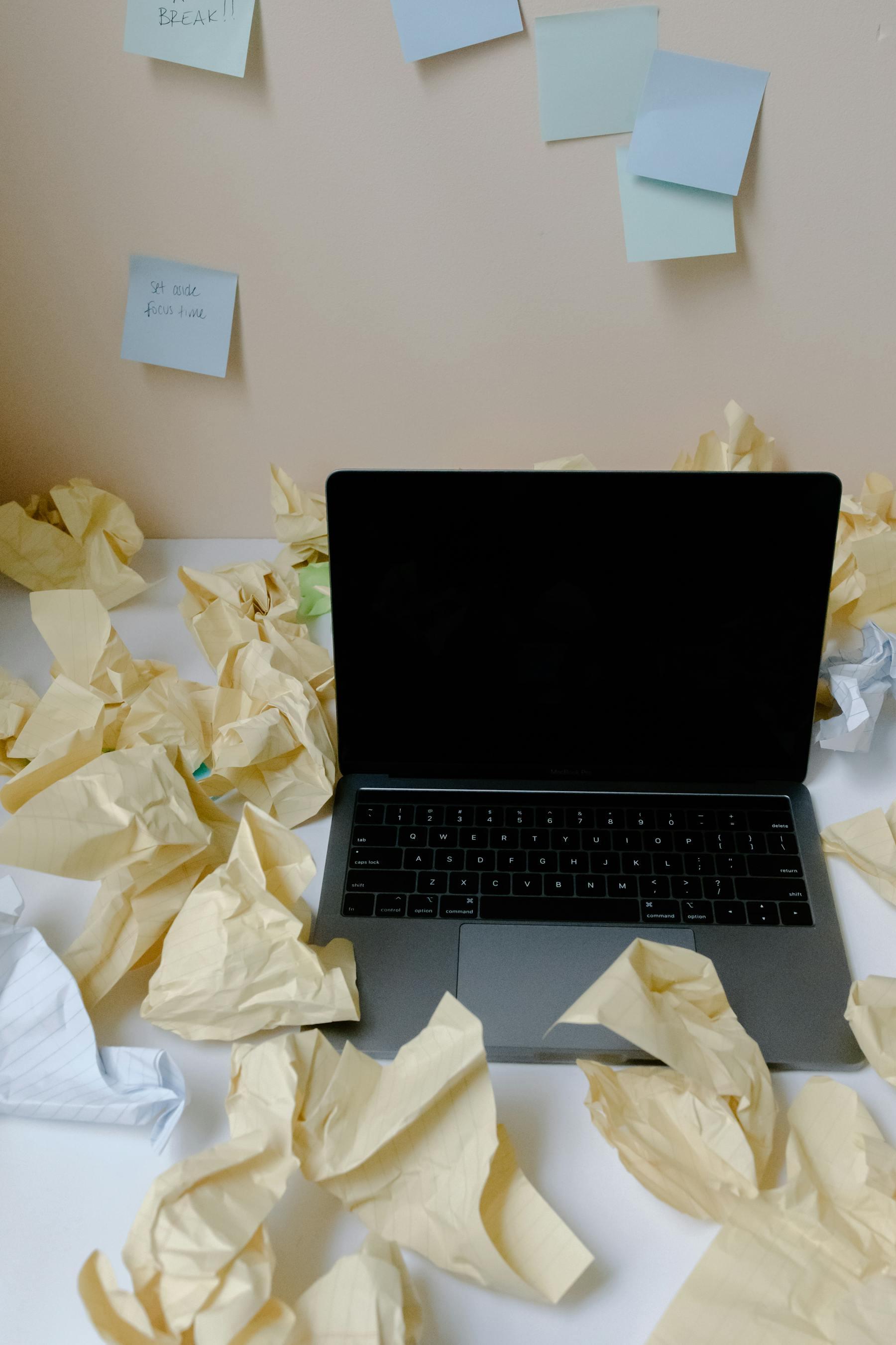 Laptop surrounded by crumpled paper and sticky notes, representing manual operational work.